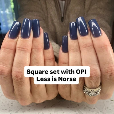 Nails with navy blue polish held by a person, with text overlay 'Square set with OPI Less is Norse'.