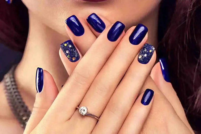 Manicured nails painted in deep navy blue with sparkly accent nails.