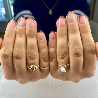Two hands wearing gold rings with gemstones on a neutral background
