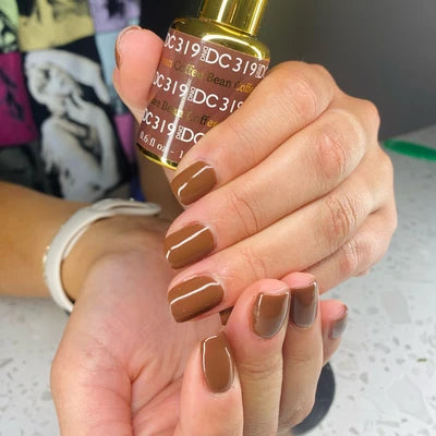 Hand holding a bottle of nail polish with brown nail polish on nails