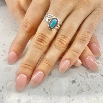 Hand wearing a silver ring with a turquoise stone on a light background