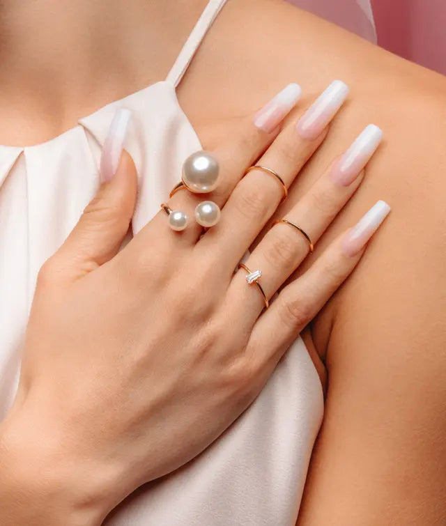 Hand wearing multiple pearl and gold rings on a blurred background