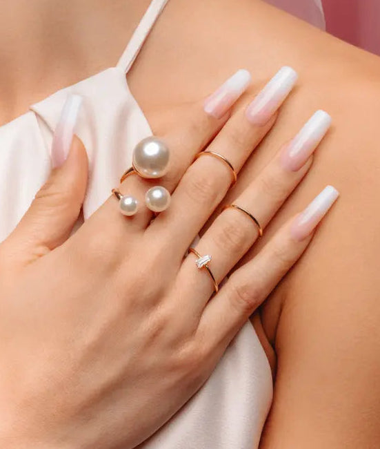 Hand wearing multiple pearl and gold rings on a blurred background