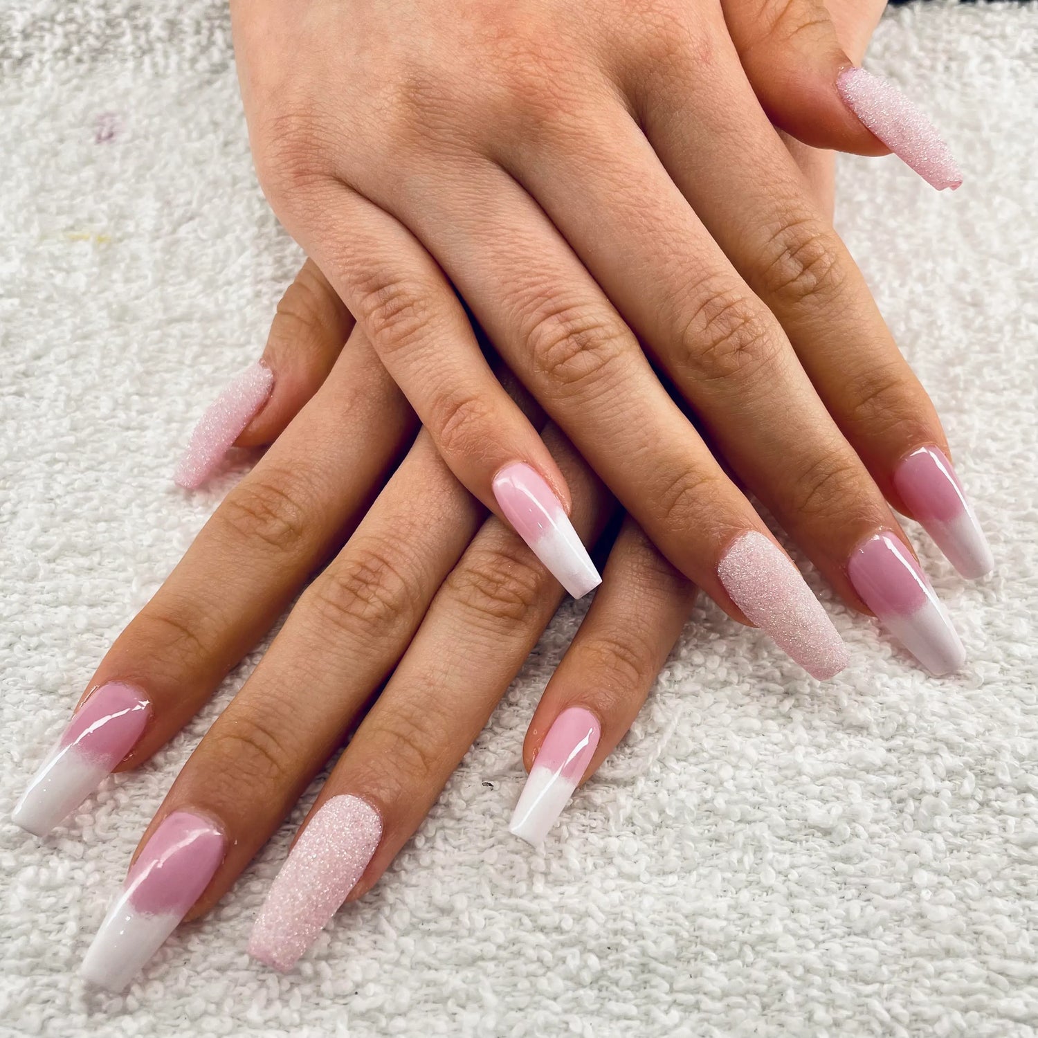 Close-up of hands with pink and white gradient nails on a textured surface